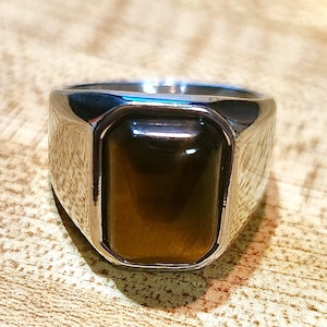 May include: A silver ring with a brown tiger's eye gemstone set in a rectangular bezel.