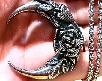 Può includere: Un ciondolo a forma di mezzaluna d'argento con un designo floreale dettagliato, tra cui una grande rosa, e una collana a catena.