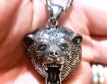 May include: A silver bear head pendant necklace with a detailed, snarling expression. The pendant is attached to a silver chain.