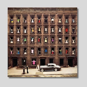 Può includere: Una fotografia vintage di un edificio in mattoni marroni con più finestre. Donne in abiti colorati sono in piedi alle finestre, guardando fuori. Un'auto argentata è parcheggiata davanti all'edificio.