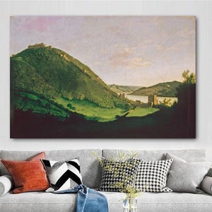 May include: A landscape painting depicts a green, grassy hill with a castle on top. The painting has a light blue sky and a river in the background. The artwork is displayed above a gray sofa with colorful pillows.