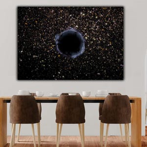 May include: A large canvas print depicting a black hole in space, surrounded by a swirling galaxy of stars. The artwork is displayed above a wooden dining table with brown chairs.