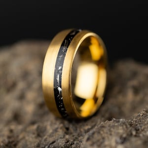May include: A gold ring with a black and white inlay. The ring is sitting on a rough, textured surface.