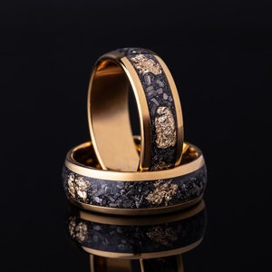 May include: Two gold rings with a black and gold speckled design. The rings are stacked on top of each other.