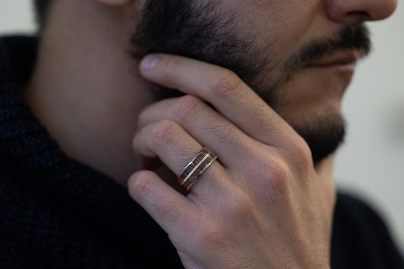 K&ouml;nnte beinhalten: Ein Holzring mit zwei silbernen B&auml;ndern. Der Ring wird am Finger einer Person getragen.
