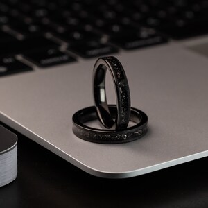 K&ouml;nnte beinhalten: Zwei schwarze Ringe mit einer strukturierten Oberfl&auml;che, &uuml;bereinander gestapelt, auf einem silbernen Laptop.
