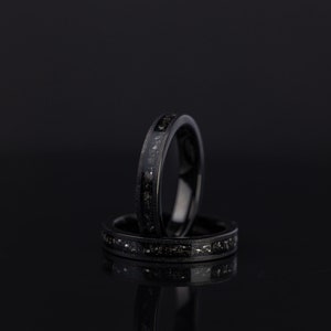 K&ouml;nnte beinhalten: Zwei schwarze Ringe mit einem d&uuml;nnen Band aus silbernem Glitzer. Die Ringe sind &uuml;bereinander gestapelt.