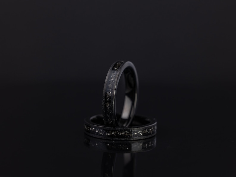 K&ouml;nnte beinhalten: Zwei schwarze Ringe mit einem d&uuml;nnen Band aus silbernem Glitzer. Die Ringe sind &uuml;bereinander gestapelt.