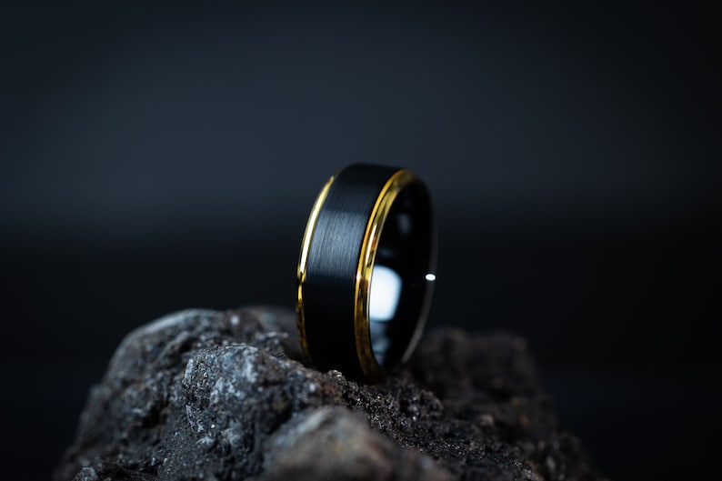 May include: A black tungsten carbide ring with a brushed finish and a gold band around the edge.