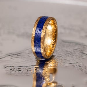 May include: A gold ring with a blue inlay. The ring has a textured surface and is set against a silver background.