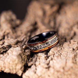 Peut inclure: Une bague en carbure de tungst&egrave;ne noir avec un incrustation en bois. L'incrustation pr&eacute;sente un motif de bois brun et or avec un accent en m&eacute;tal argent&eacute;.