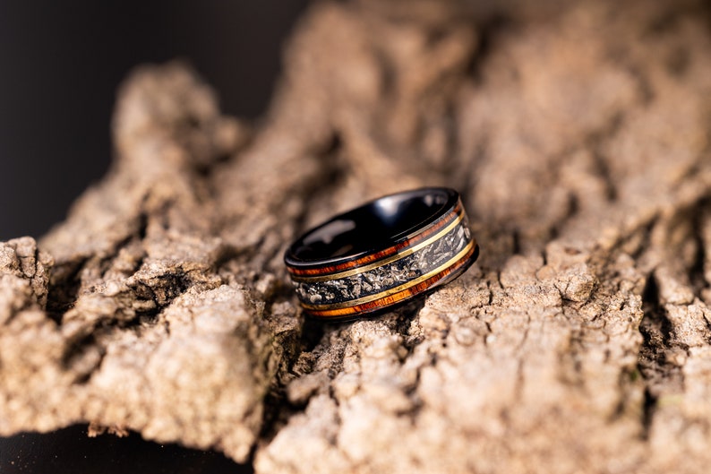 Peut inclure: Une bague en carbure de tungst&egrave;ne noir avec un incrustation en bois. L'incrustation pr&eacute;sente un motif de bois brun et or avec un accent en m&eacute;tal argent&eacute;.