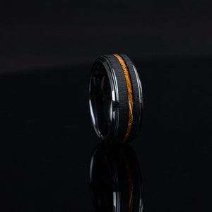 May include: A black tungsten carbide ring with a thin band of wood inlay.