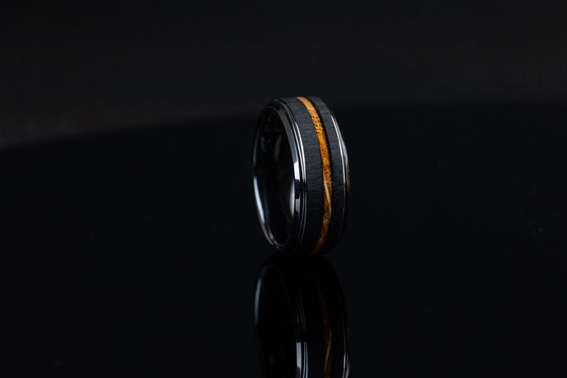 May include: A black tungsten carbide ring with a thin band of wood inlay.
