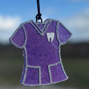 May include: Purple scrub top ornament with silver glitter accents and a white tooth graphic.