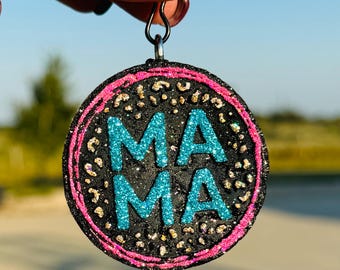 May include: A round, black, glittery earring with a pink border. The word "MAMA" is written in turquoise glitter.