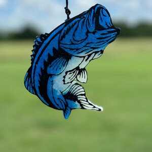 May include: A blue and black bass fish cutout hanging from a black string. The fish is in a jumping position with its mouth open.
