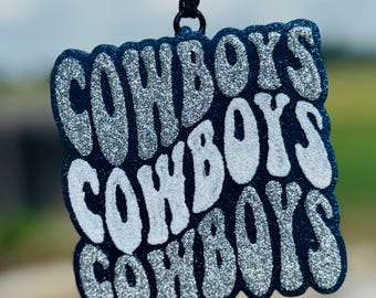 May include: A blue and silver glitter ornament with the word "COWBOYS" repeated three times in a retro font.