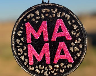 May include: A round, black and gold glitter ornament with the word "MAMA" in pink glitter letters.
