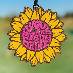May include: A yellow glitter sunflower with a pink glitter center that says "You Are My Sunshine".