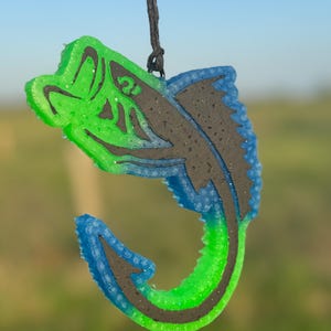 May include: A green and blue fish-shaped car air freshener with a black string for hanging. The fish is in a jumping position with its mouth open.