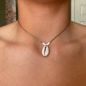 May include: A simple brown cord necklace with white beads and a white seashell pendant.