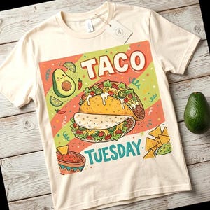 Könnte beinhalten: Cremefarbenes T-Shirt mit einem farbenfrohen Taco-Motiv. Das Design zeigt das Wort "TACO" in Rot und "TUESDAY" in Türkis, sowie Illustrationen von Avocado, Limettenscheiben und Chips mit Salsa und Guacamole.