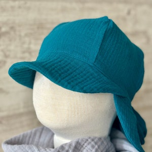 Puede incluir: Un sombrero de pescador color verde azulado hecho de una tela texturizada y arrugada. El sombrero presenta un ala ancha inclinada hacia abajo y una copa redondeada. Se muestra sobre una cabeza de maniqu&iacute; color hueso, con una tela gris suave drapeada en la base.