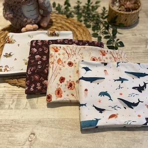 May include: Four fabric squares featuring different patterns. The first square has a white background with brown and green illustrations of woodland creatures. The second square has a brown background with a floral pattern. The third square has a cream background with a floral pattern in shades of orange and brown. The fourth square has a white background with a blue and white pattern of sea creatures.
