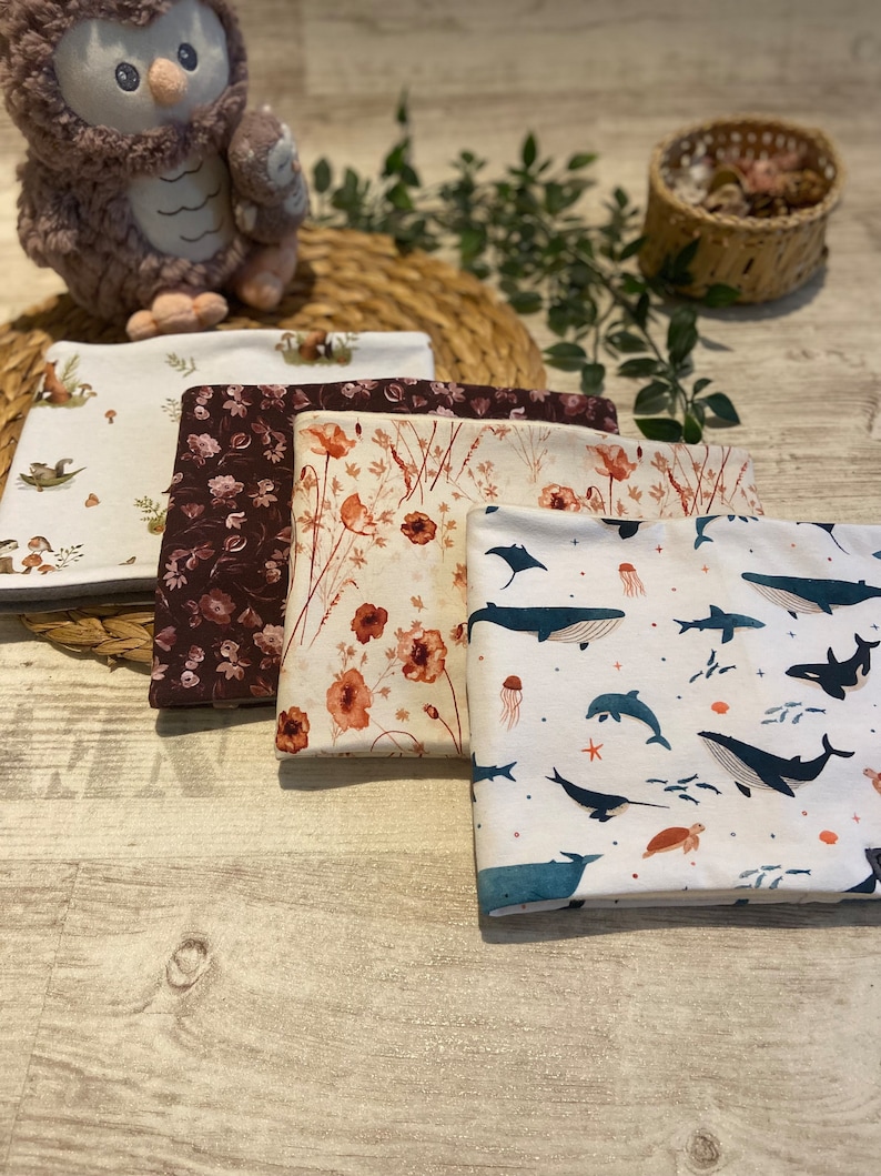 May include: Four fabric squares featuring different patterns. The first square has a white background with brown and green illustrations of woodland creatures. The second square has a brown background with a floral pattern. The third square has a cream background with a floral pattern in shades of orange and brown. The fourth square has a white background with a blue and white pattern of sea creatures.