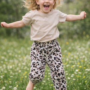 Op de afbeelding: Een beige T-shirt met korte mouwen gecombineerd met een losvallende broek met een zwart, bruin en wit luipaardpatroon. De broek heeft een elastische tailleband en elastische boorden bij de enkels voor een comfortabele pasvorm.