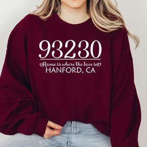 May include: Maroon sweatshirt with the text "93230 Home is where the love in HANFORD, CA" in white. The sweatshirt is a solid maroon color.