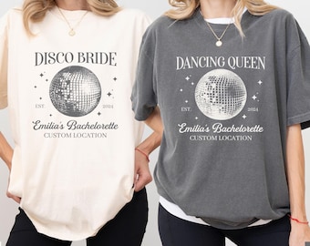 May include: Two t-shirts with a disco ball graphic and text that says "Disco Bride" and "Dancing Queen". The text also includes "Est. 2024" and "Emilia's Bachelorette" with a custom location.