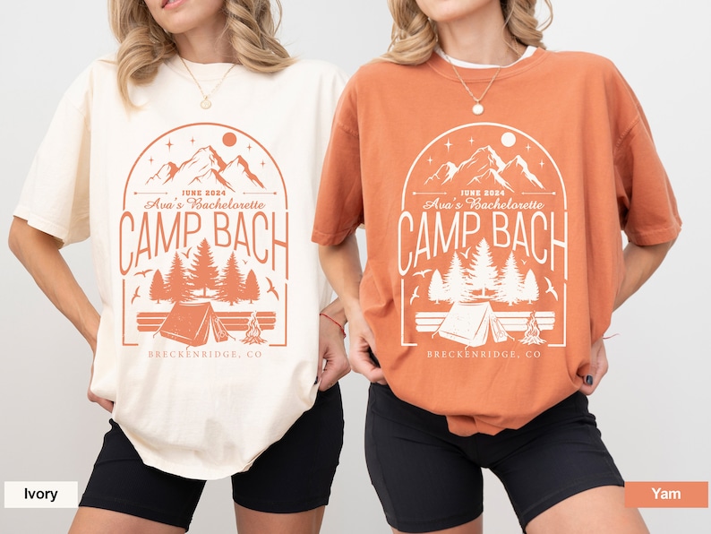 May include: Two t-shirts with a camping theme design. The design features a mountain range, trees, a tent, and a campfire. The text on the shirts reads "JUNE 2024 Ava's Bachelorette CAMP BACH BRECKENRIDGE, CO". One shirt is ivory and the other is orange.