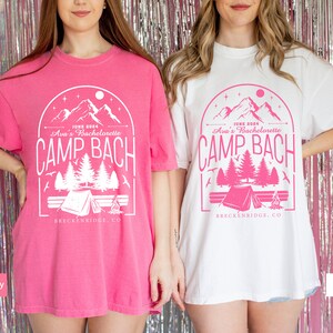 May include: Two oversized t-shirts with a pink and white mountain scene graphic. The graphic says "June 2024 Ava's Bachelorette Camp Bach Breckenridge, CO". One shirt is pink and the other is white.
