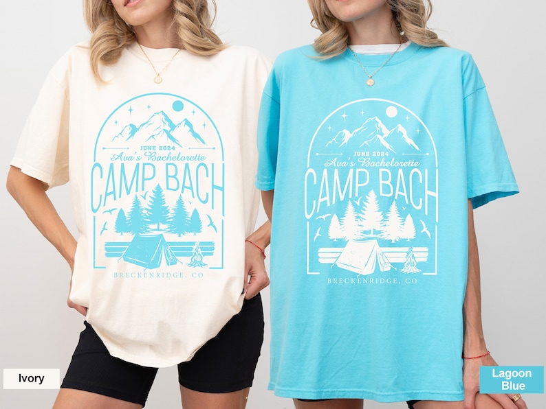 May include: Two oversized t-shirts with a graphic design of a mountain range, trees, a tent, and a campfire. The text on the shirts reads "June 2024 Ava's Bachelorette Camp Bach Breckenridge, CO". The shirt on the left is ivory and the shirt on the right is lagoon blue.