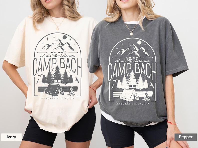 May include: Two oversized t-shirts with a camping theme. The shirts are in ivory and pepper colors. The design features a mountain range, trees, a tent, a campfire, and the text "JUNE 2024 Ava's Bachelorette CAMP BACH BRECKENRIDGE, CO".