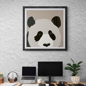 May include: A framed illustration of a panda bear's face with black and white fur. The panda is looking directly at the viewer. The frame is black and the background is a light brown color. The image is hanging on a white wall above a desk with a computer, laptop, and other office supplies.
