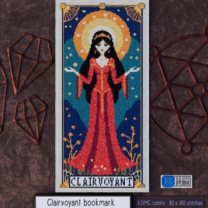 Pode incluir: Um marcador de página de ponto cruz com uma mulher em um vestido vermelho com uma coroa, cercada por estrelas e flores. O texto "Clairvoyant" está na parte inferior do marcador de página.