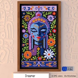 May include: A cross-stitch pattern of a woman's face with flowers and leaves surrounding her. The woman has blue skin and closed eyes. The background is black. The title "Dreamer" is below the image. The text "13 DMC colors 81 x 143 stitches" is below the title.