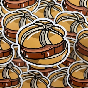 May include: A set of illustrated stickers featuring a cartoon depiction of a German pretzel roll filled with a meaty sausage. The stickers are white with a black outline and feature a variety of colors, including brown, yellow, and red.