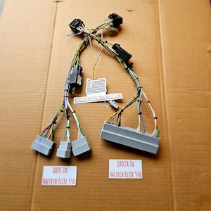 May include: A close-up of two wiring harnesses with multiple connectors. The harnesses are labeled "OBD1 to Haltech Elite 550" and "OBD2A to Haltech Elite 550". The harnesses are wired with a variety of colored wires.
