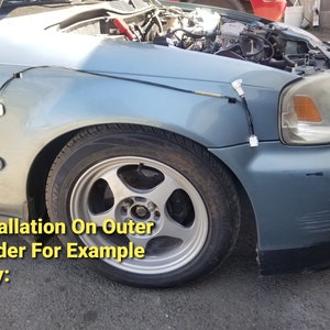 May include: A close-up of a gray car with a black wire running along the fender. The car has a silver rim and the text "Installation On Outer Fender For Example Only:" is visible in the image.