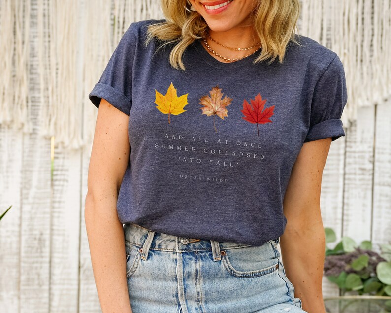 Puede incluir: Una camiseta azul marino con un gr&aacute;fico de tres hojas de oto&ntilde;o y la cita "Y de repente el verano se derrumb&oacute; en oto&ntilde;o." de Oscar Wilde.