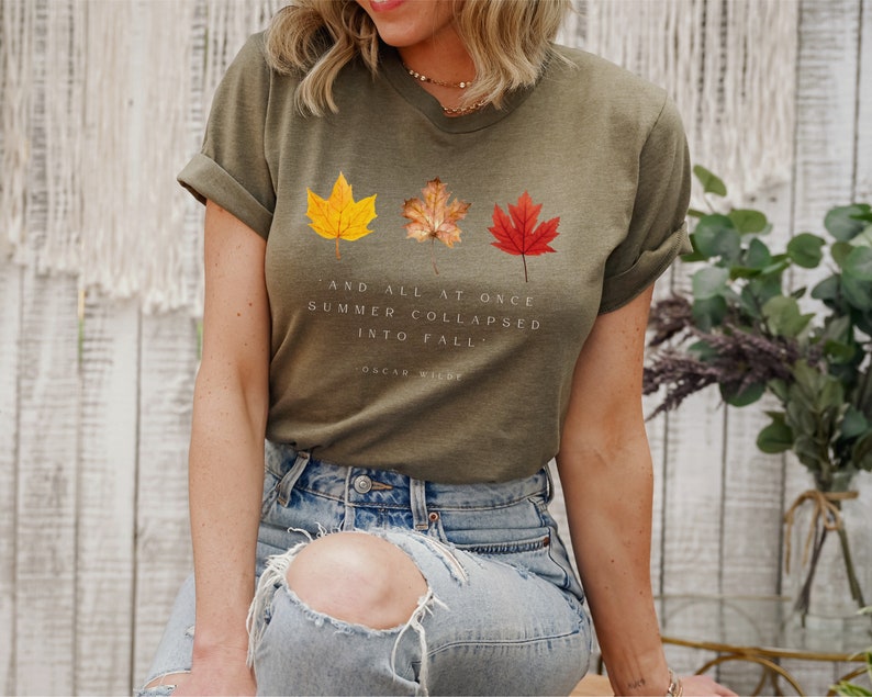 Puede incluir: Una camiseta verde con un gr&aacute;fico de tres hojas de oto&ntilde;o y el texto "And all at once summer collapsed into fall." - Oscar Wilde.
