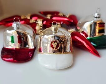 May include: A selection of baseball cap-shaped Christmas baubles. The baubles are silver and red, with gold detailing. One features the Italian flag, and another has a pizza slice emblem. Other red baubles are in the background.
