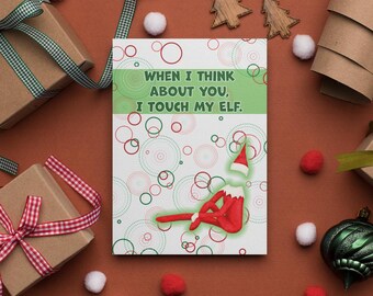 May include: A greeting card with the text "When I think about you, I touch my elf." The card features a cartoon elf design in red and white, with a green and white background. The card is surrounded by gift boxes, ornaments, and decorative elements.