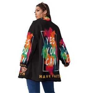 May include: Black jacket with colorful paint-like accents and the text "YES YOU CAN HAVE FAITH". The jacket has long sleeves with the same colorful design and a frayed hem. The model is wearing blue jeans.