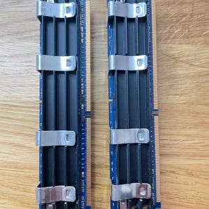 May include: Two blue RAM memory modules with silver metal clips. The modules have black vertical fins and gold-colored connectors along one edge. The modules are designed for use in computers and other electronic devices.
