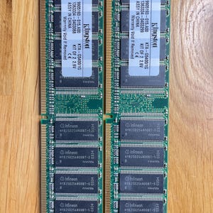 May include: Four green circuit boards with black text and labels. The text on the labels reads "Kingston", "KTA-G5400/1G", "KIT OF 2 2.6V", "9905193-015.A00", "1363334-0403068", "ASSY IN CHINA", "Warranty Void If Removed", "Infineon", "HYB250256800BT-5", "0334", "FVV47056".